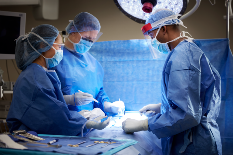 Three surgeons in blue scrubs and surgical masks performing a medical procedure.