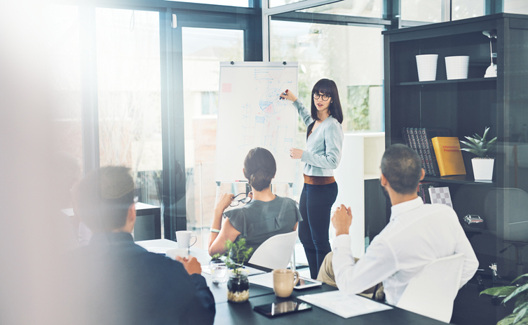 A woman confidently presenting to a group of attentive individuals during a professional meeting.