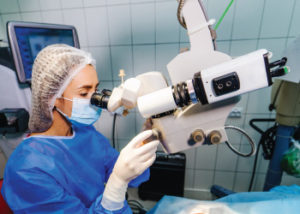 A woman in a blue uniform using an ophthalmic device to examine a patient's eyes.