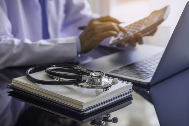 Medical professional checking laptop with stethoscope.