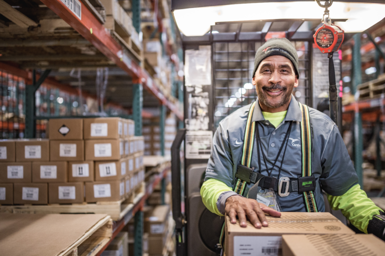 Warehouse employee grinning while carrying box.
