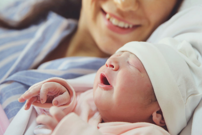A woman joyfully cradles a newborn baby in her arms, both sharing a heartwarming smile of pure happiness.