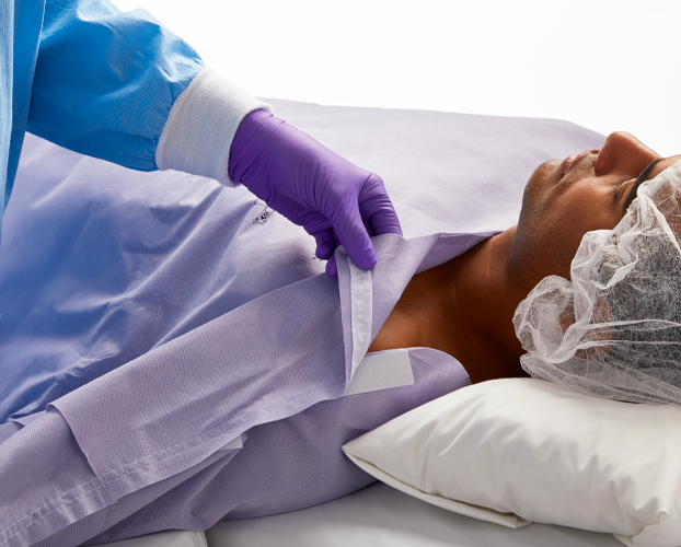 Person lying down on a hospital bed with purple gown.