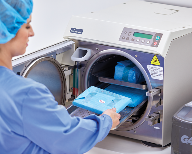 A woman in blue scrub suit placing a bag into a machine.